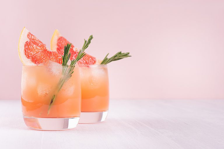 Summer cold cocktail with ice cubes, juice and slices grapefruit on pastel pink background