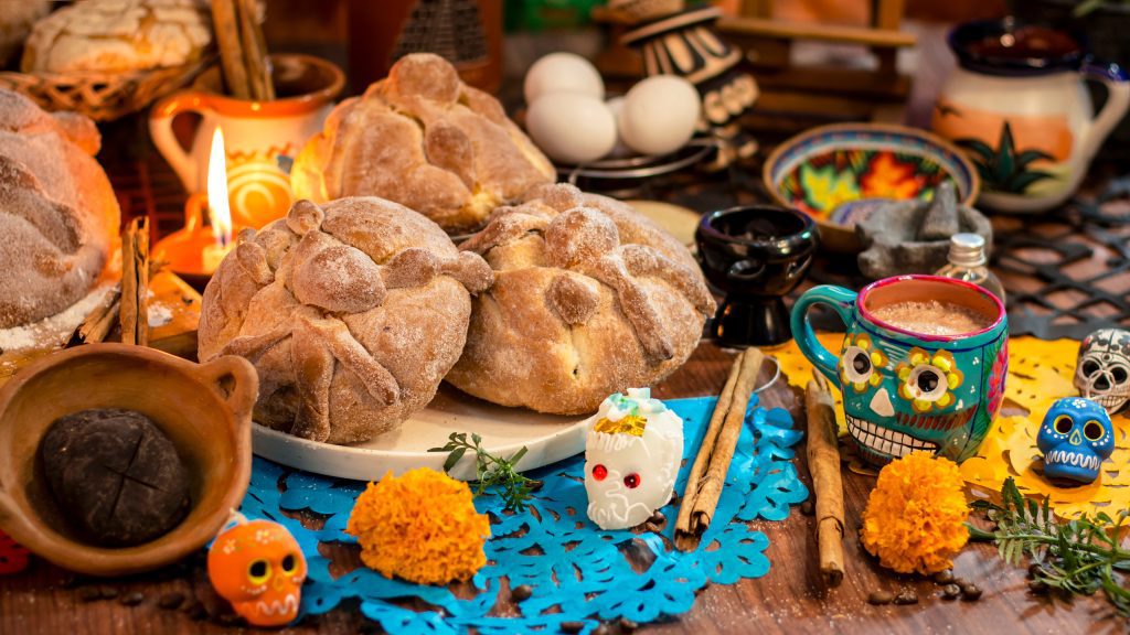 Alimentación en el Día de Muertos con pan de muerto, frutas, velas y flores de cempasúchil en una ofrenda tradicional mexicana.
